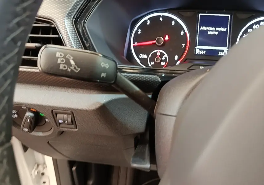 Vue intérieure du tableau de bord du Volkswagen T-Cross blanc, avec compteur et commandes au volant visibles.