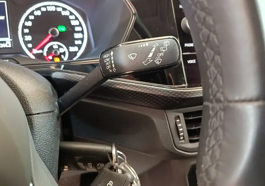 Gros plan sur la manette d’essuie-glace à gauche du volant cuir du Volkswagen T-Cross blanc, tableau de bord en arrière-plan.