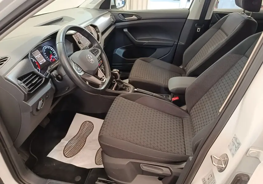 Vue intérieure côté conducteur du Volkswagen T-Cross blanc, montrant sièges tissu gris et tableau de bord moderne.