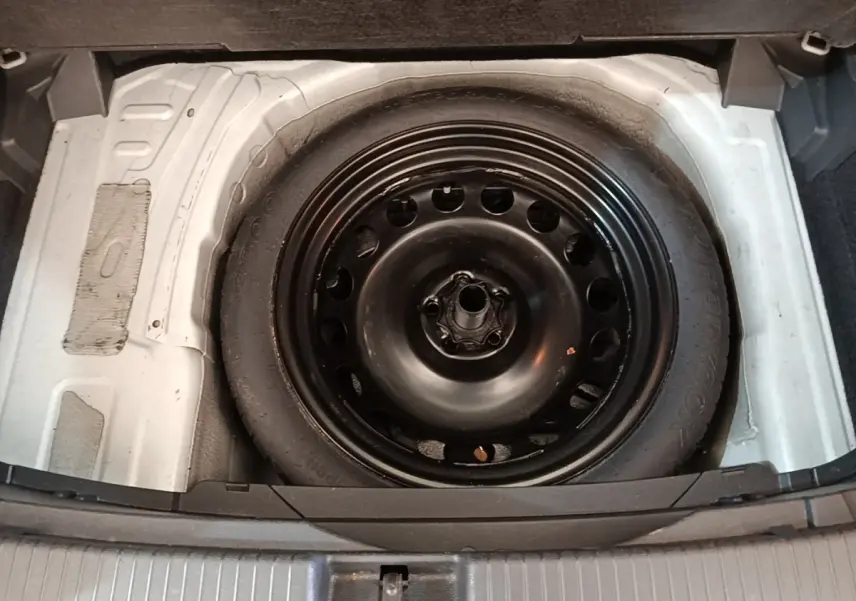 Roue de secours galette noire dans le coffre d’un Volkswagen T-Cross blanc, vue plongeante sur le compartiment.