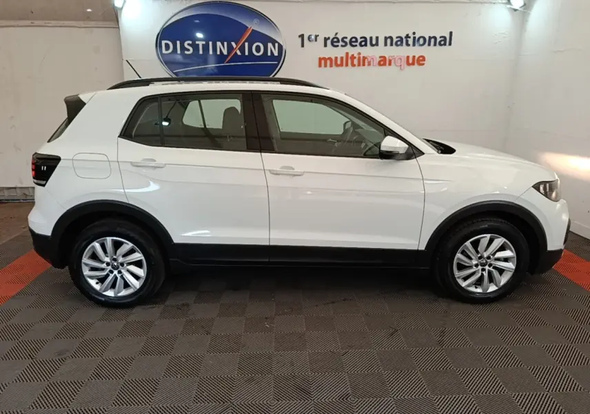 Vue de profil côté gauche d'un Volkswagen T-Cross blanc 2022 avec jantes alliage et barres de toit noires.