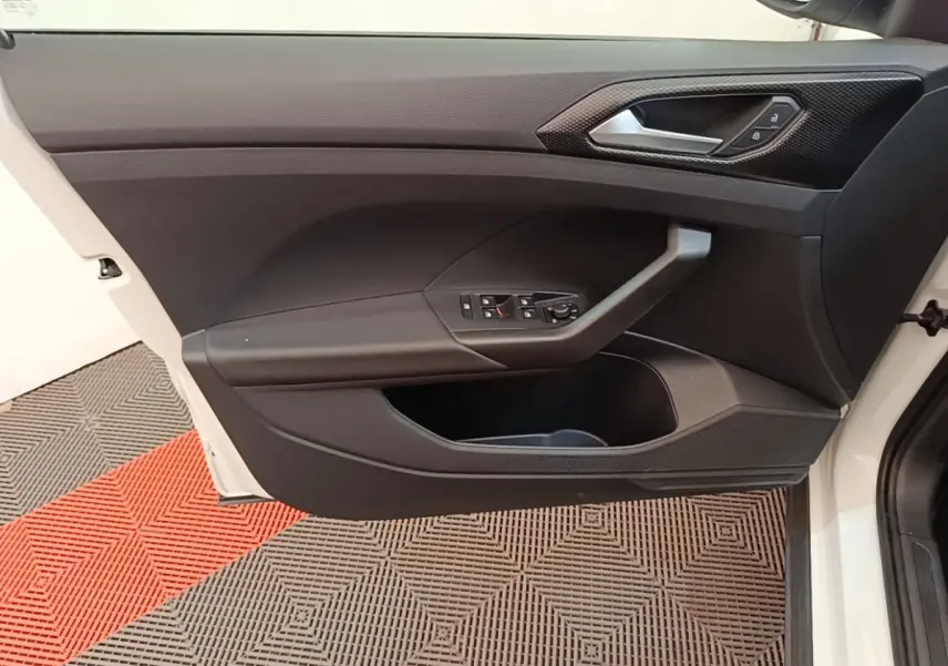Vue de profil intérieur sur la porte avant gauche blanche du Volkswagen T-Cross avec commandes de vitres et poignée grise.