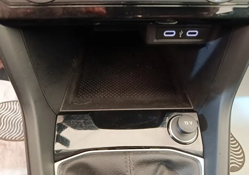 Gros plan sur la console centrale du Volkswagen T-Cross 2022, montrant les ports USB et la prise 12V avec finition noire brillante.
