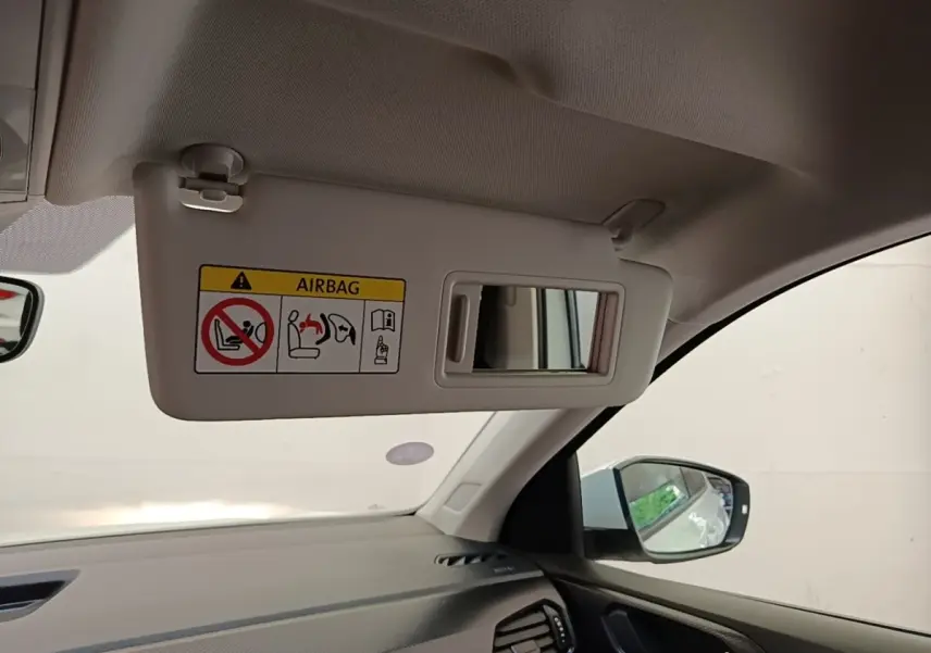 Détail intérieur du pare-soleil côté conducteur avec miroir et avertissement airbag du Volkswagen T-Cross blanc.