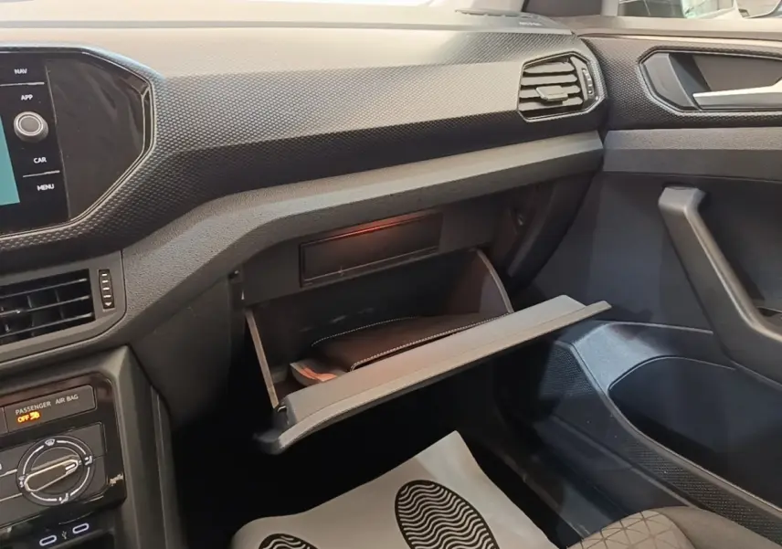 Intérieur du Volkswagen T-Cross 2022, vue côté passager avec boîte à gants ouverte et tableau de bord noir texturé.