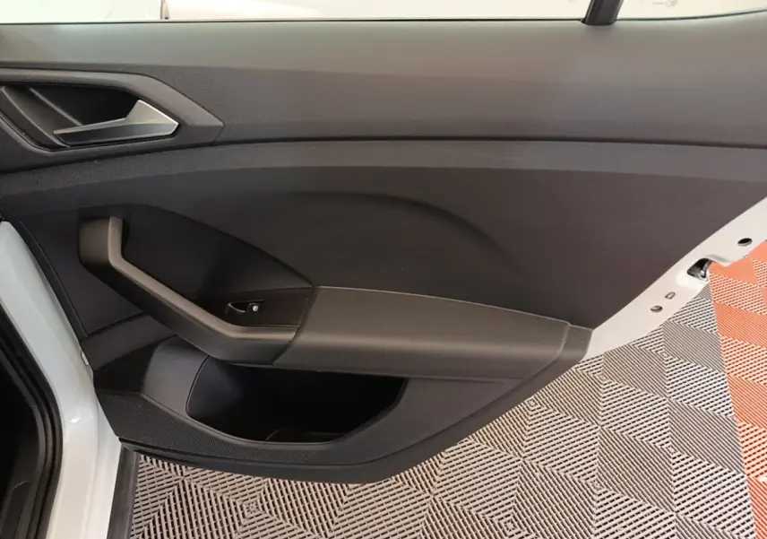 Intérieur côté gauche de la porte avant blanche du Volkswagen T-Cross 2022 avec poignée noire et bouton de vitre électrique.