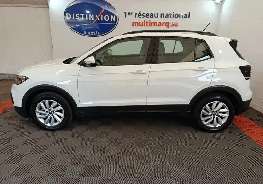 Profil droit d'un Volkswagen T-Cross blanc 2022 avec jantes alliage et barres de toit noires en intérieur showroom.