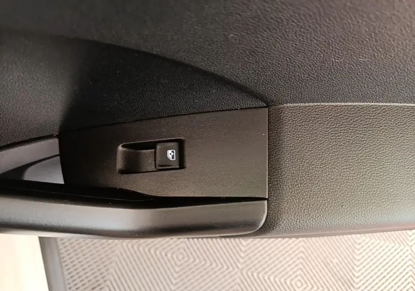 Gros plan sur le bouton de commande de lève-vitre côté porte intérieure d’un Volkswagen T-Cross blanc.