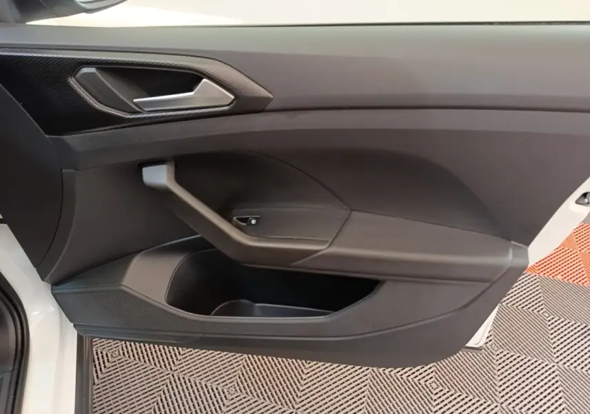 Vue intérieure côté gauche de la porte avant d’un Volkswagen T-Cross blanc avec poignée argentée et rangement intégré.