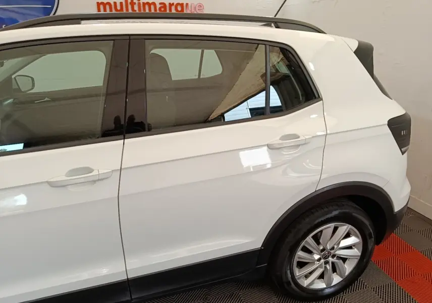 Vue latérale droite d'un Volkswagen T-Cross blanc, mettant en valeur la roue arrière et les vitres teintées.