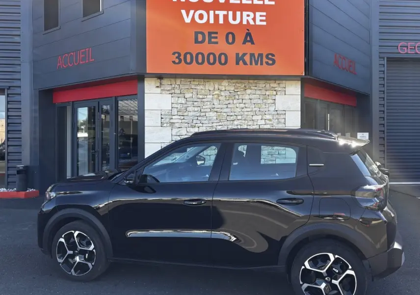 Profil côté gauche d'une Citroën C3 Turbo 100 BVM6 MAX noire, avec jantes distinctives, devant un bâtiment commercial.