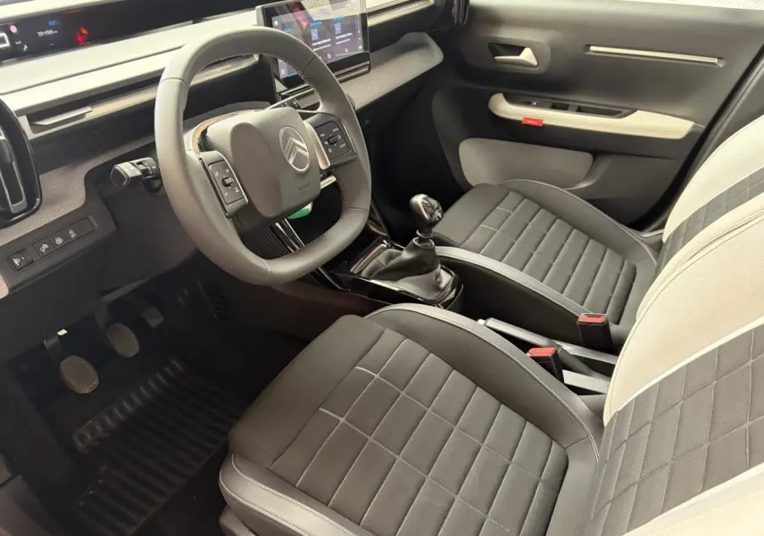 Vue intérieure côté conducteur de la Citroën C3 2025 noire, avec volant cuir, écran tactile et sièges bi-ton gris et beige.