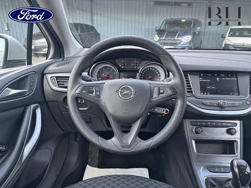 Vue intérieure centrée sur le volant Opel d'une Astra 1.2 Turbo gris Mineral, avec tableau de bord et écran tactile visible.