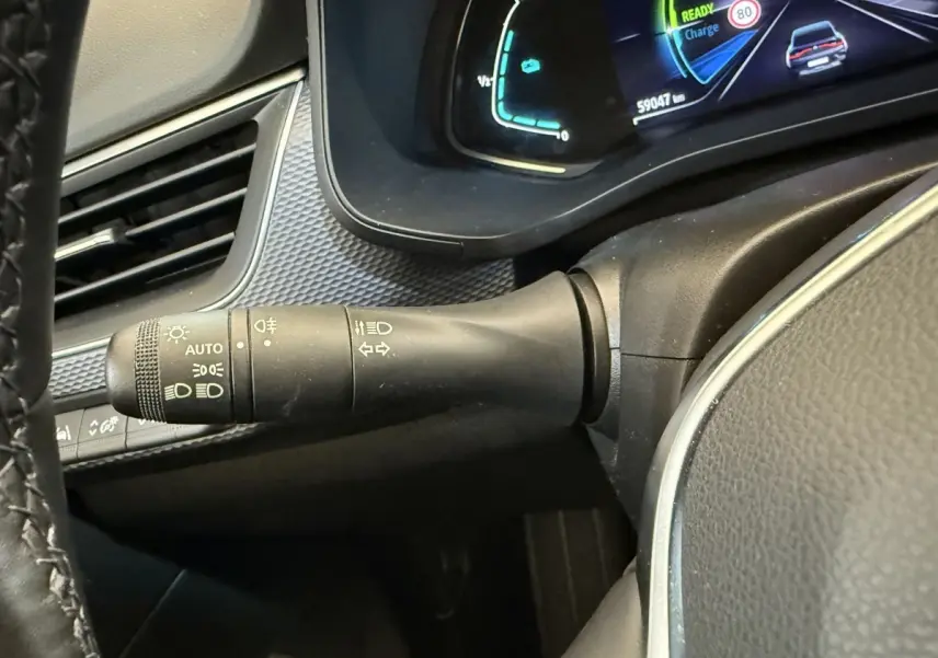 Gros plan sur la manette de commandes d’éclairage et clignotants, tableau de bord numérique bleu et noir visible côté gauche.