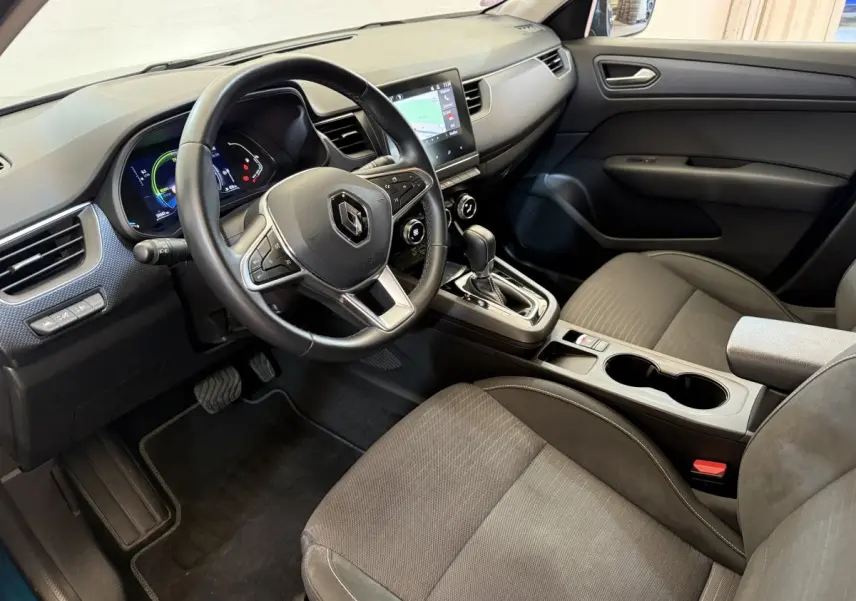 Vue intérieure côté conducteur de la Renault Arkana Business E-TECH 145 avec volant multifonctions et écran tactile central.