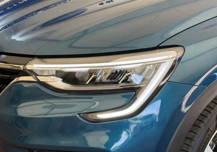 Gros plan sur le phare avant droit du Renault Arkana bleu, mettant en valeur la signature lumineuse LED en forme de C.