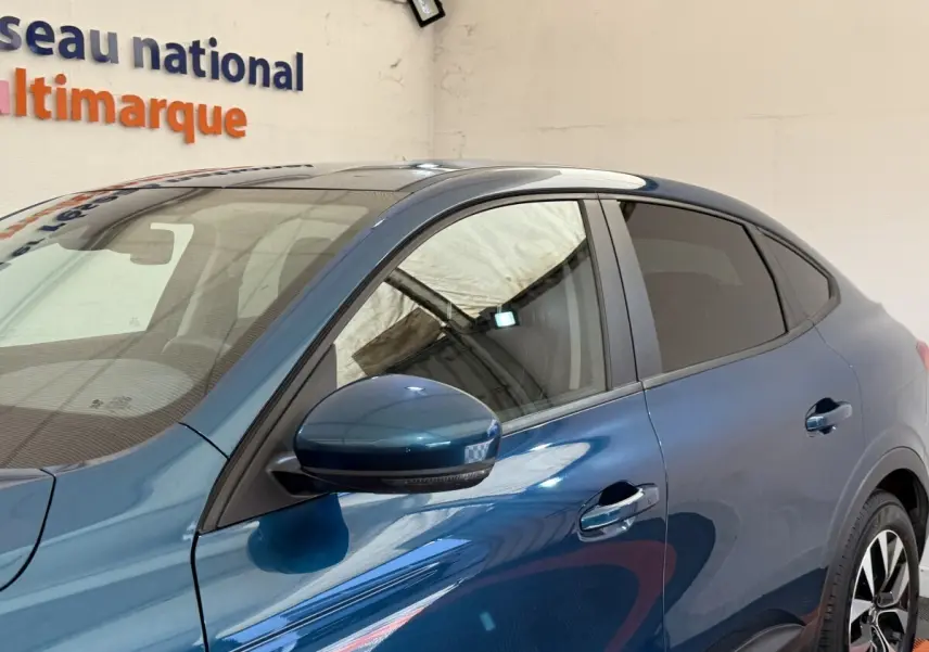 Vue de côté droit sur la partie avant d’une Renault Arkana Business E-TECH 145 bleu avec rétroviseur et poignées visibles.