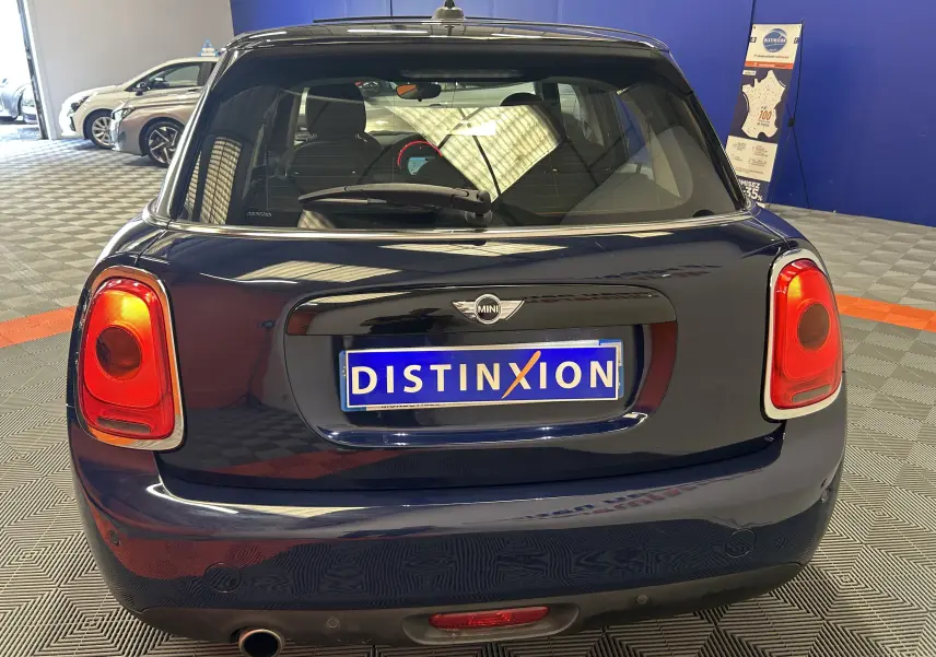 Vue arrière d'une MINI 5 portes bleu foncé avec feux rouges et toit ouvrant visible en intérieur showroom.