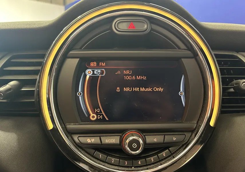 Gros plan sur l’écran central rond du tableau de bord de la MINI 5P bleu, affichant la radio NRJ 100.6 MHz.
