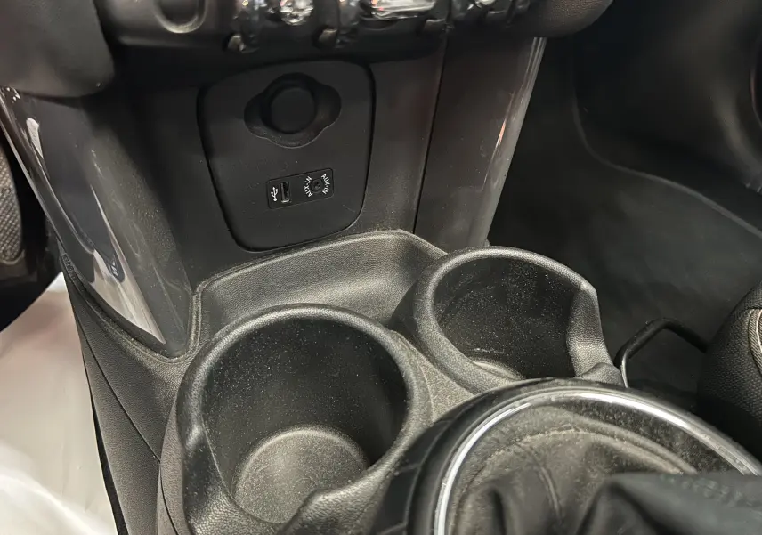 Gros plan sur la console centrale noire de la MINI 5P Cooper D 2015, montrant porte-gobelets et prises USB/AUX.
