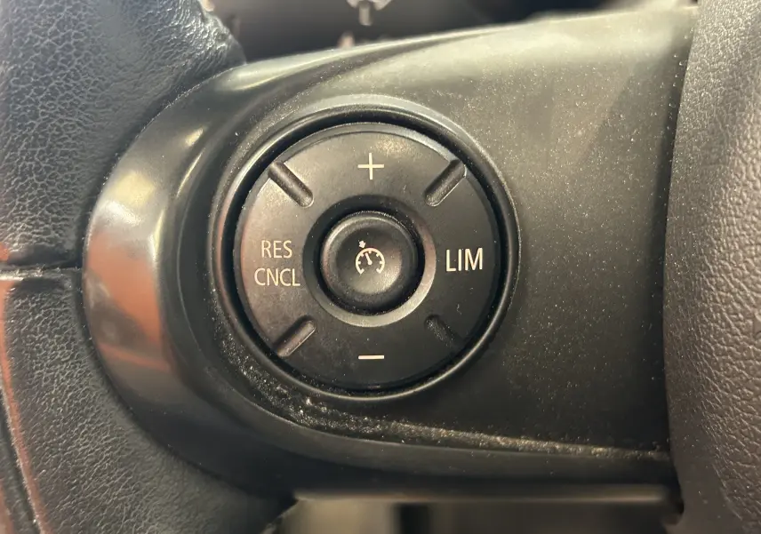 Gros plan sur les commandes de régulateur de vitesse sur le volant noir d'une MINI 5P Cooper D bleu de 2015.