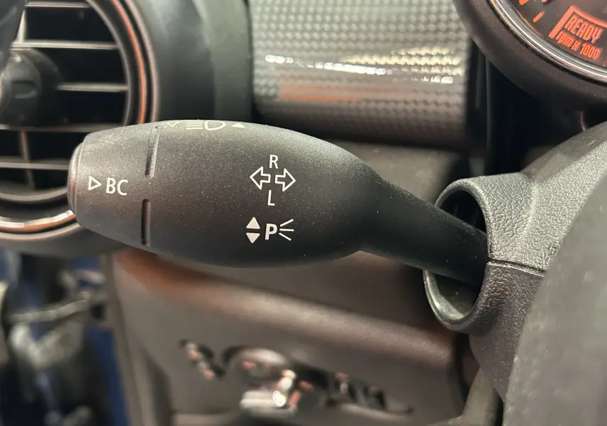 Gros plan sur la manette de clignotant noire à gauche du volant dans l’habitacle bleu d’une MINI 5 portes.