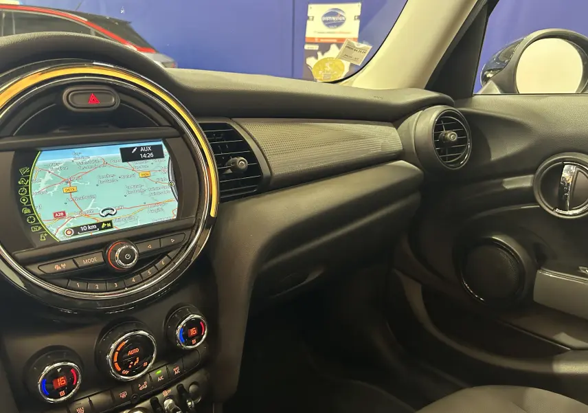 Vue intérieure côté passager du tableau de bord de la MINI 5P Cooper D 2015 avec écran GPS et commandes de climatisation.
