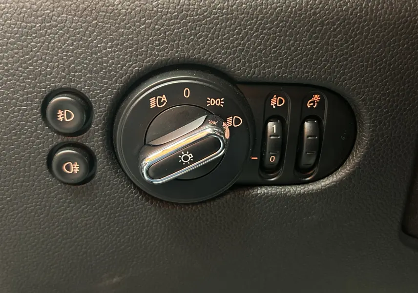 Gros plan sur la molette de réglage des phares et boutons de feux antibrouillard d'une MINI 5P bleu de 2015.