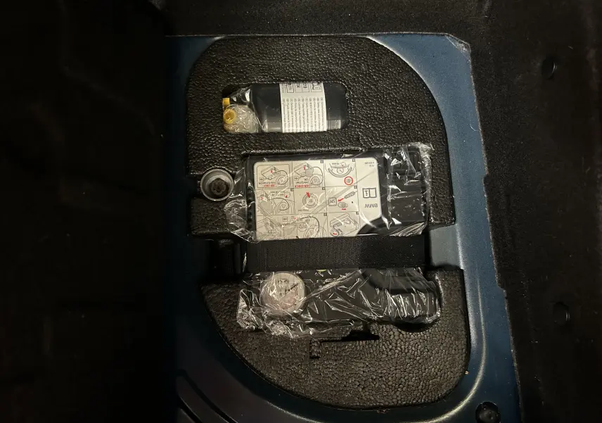 Gros plan sur le coffre d’une MINI 5P Cooper D bleu, montrant le kit de réparation pneu rangé dans un compartiment.