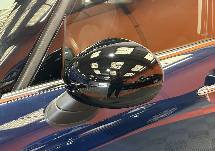 Gros plan sur le rétroviseur extérieur noir côté gauche d'une MINI 5P Cooper D bleu, avec reflet intérieur cuir marron.