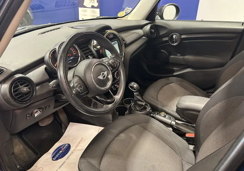 Vue intérieure côté conducteur de la MINI 5 portes Cooper D 2015, montrant le volant, tableau de bord et sièges en tissu gris.