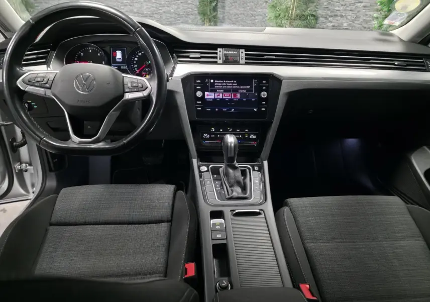 Vue intérieure avant centrée sur le tableau de bord et console centrale d'une Volkswagen Passat SW 2.0 TDI gris, avec volant cuir multifonction.