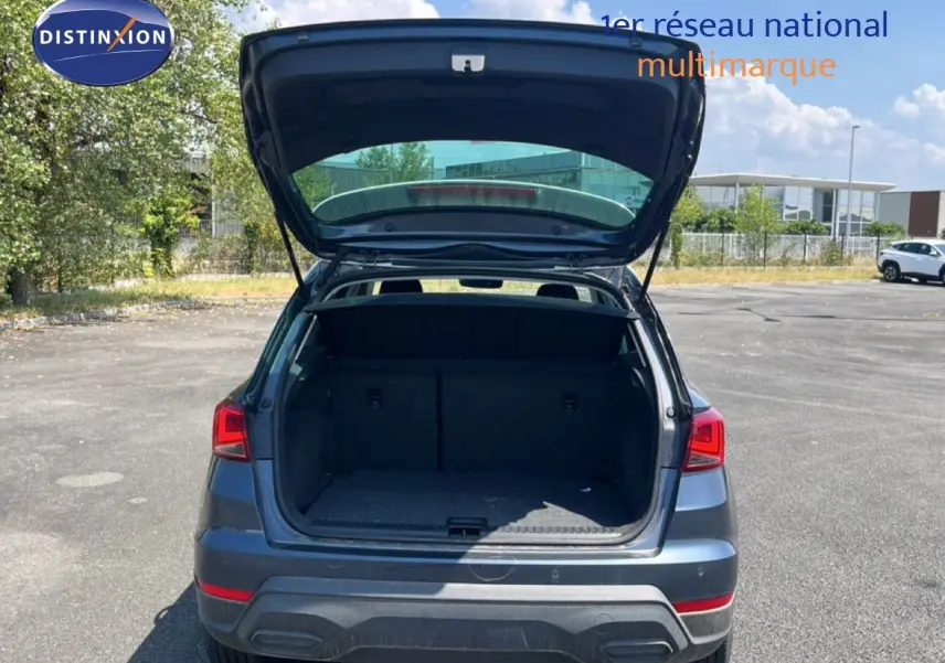 Vue arrière d'un SEAT Arona gris Magnetic avec coffre ouvert, toit blanc visible sous un ciel bleu.