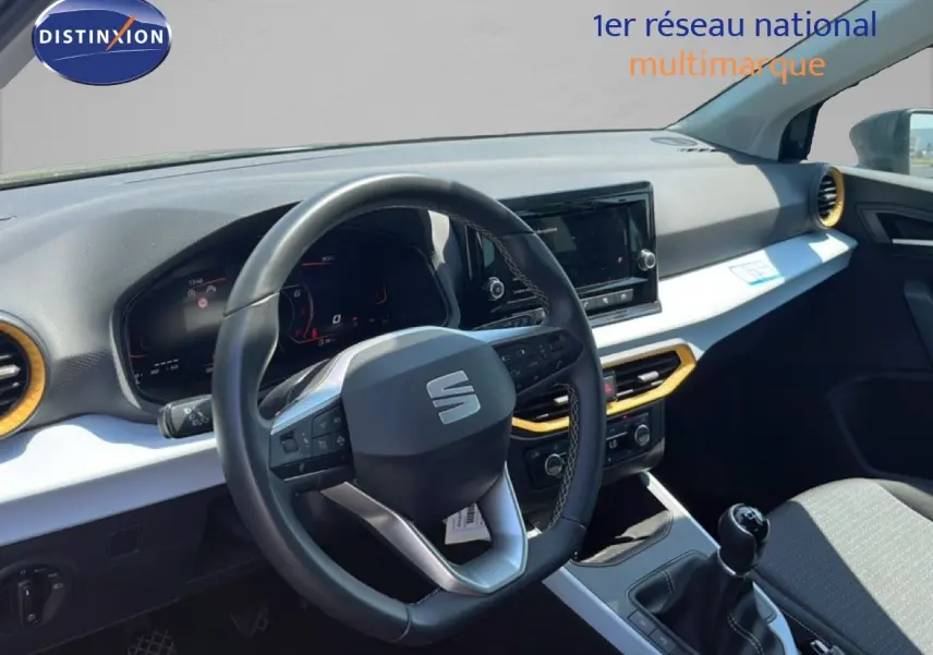 Vue intérieure côté conducteur du tableau de bord et volant d'une SEAT Arona gris magnetic avec toit blanc, boîte manuelle.