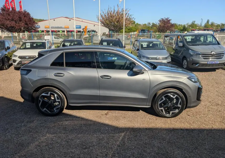 Volkswagen T-Roc gris métallisé vu de profil côté gauche, avec jantes noires et vitres surteintées.