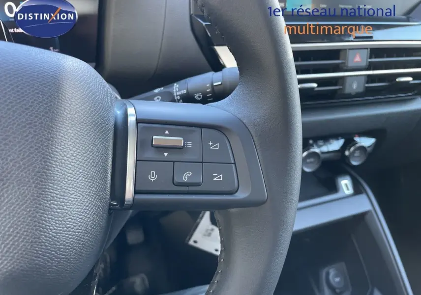 Gros plan sur les commandes au volant côté gauche d'une Citroën C4 hybride 2026, intérieur noir moderne.