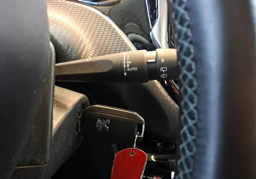 Gros plan sur la commande d'essuie-glace et la clé Peugeot insérée à gauche du volant d'un Peugeot 2008 gris de 2019.