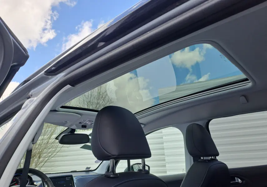 Toit panoramique en verre ouvert sur l'intérieur noir du Peugeot 2008 gris, vue depuis la porte avant gauche ouverte.