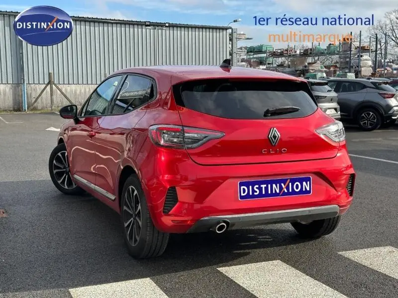 Vue 3/4 arrière droite d'une Renault Clio 1.0 TCe 90ch Techno rouge flamme avec feux arrière LED et sortie d'échappement visible.