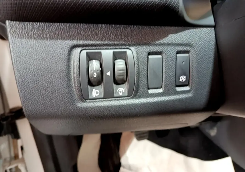 Gros plan sur les commandes de réglage des phares et du tableau de bord d’une Renault Clio Zen Energy dCi 75 blanche de 2016.