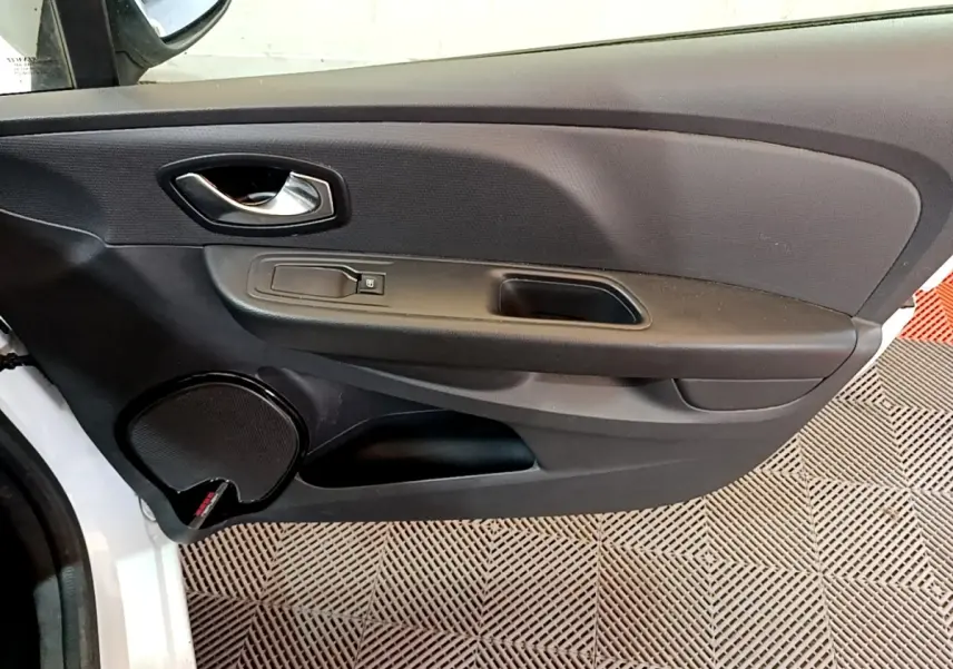 Vue rapprochée de la porte avant gauche noire d'une Renault Clio Zen Energy dCi 75 blanche, avec poignée et haut-parleur intégrés.
