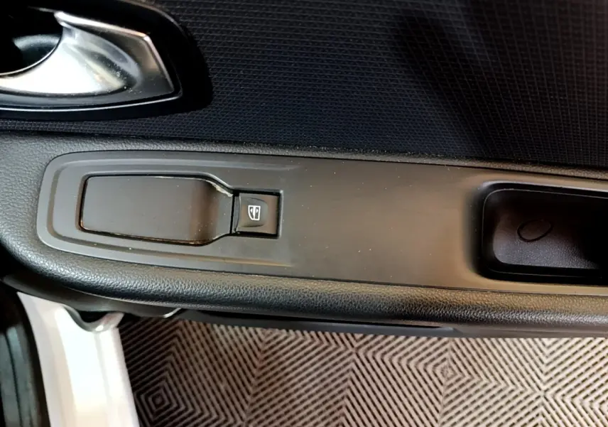 Gros plan sur la commande de lève-vitre côté conducteur de la Renault Clio blanche, avec poignée de porte noire.