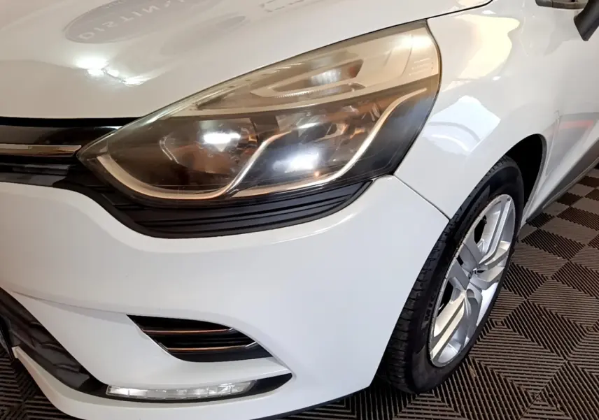 Gros plan sur l'avant droit blanc d'une Renault Clio 2016, mettant en valeur le phare et la roue alliage.