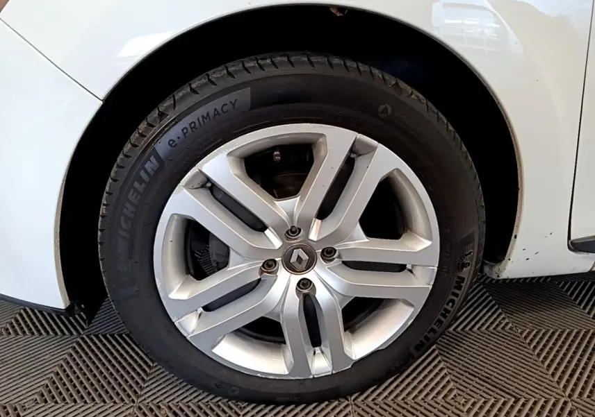 Gros plan sur la roue avant gauche d'une Renault Clio blanche, jante alliage à cinq doubles branches.