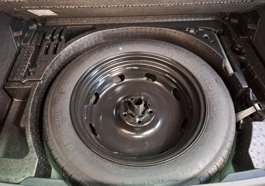 Roue de secours noire enfoncée dans le coffre du Volkswagen Tiguan 2023 Nightshade Blue, vue en plongée.