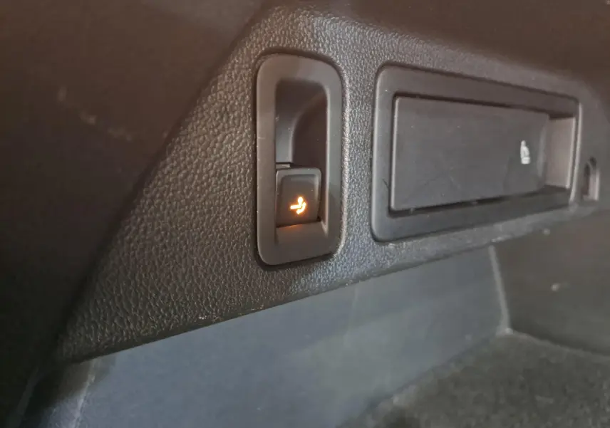 Gros plan sur le bouton de rabattement électrique des sièges dans le coffre du Volkswagen Tiguan Nightshade Blue 2023.