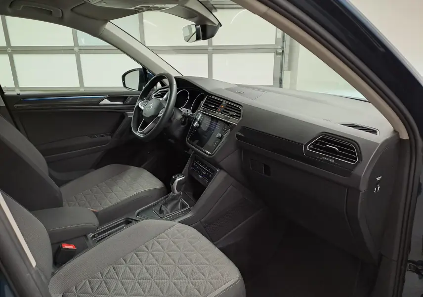 Vue intérieure côté conducteur du Volkswagen Tiguan 2023 Nightshade Blue, avec tableau de bord moderne et sièges gris à motifs.