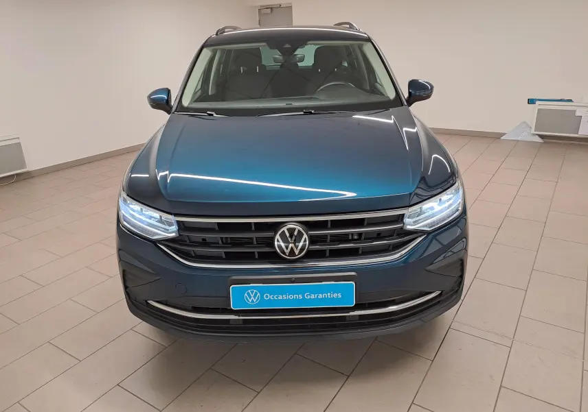 Vue de face du Volkswagen Tiguan 2023 en bleu Nightshade avec phares allumés et calandre noire brillante.
