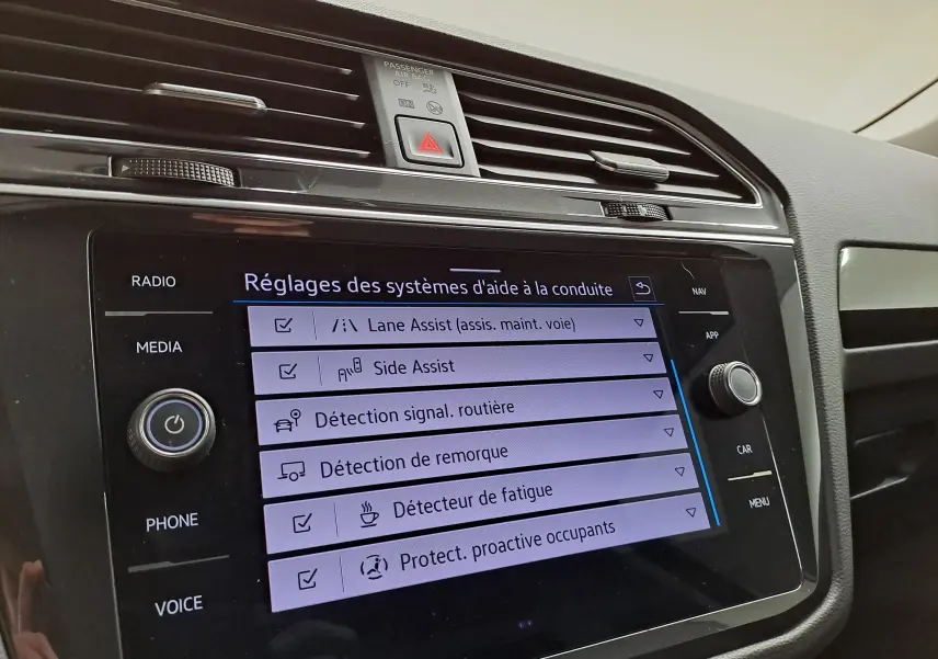 Écran tactile central du Volkswagen Tiguan 2023 affichant les réglages des aides à la conduite dans un intérieur noir.