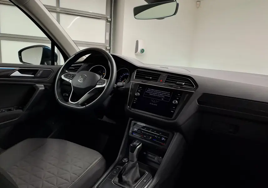 Vue intérieure côté conducteur du Volkswagen Tiguan 2023 avec tableau de bord noir et écran tactile central.